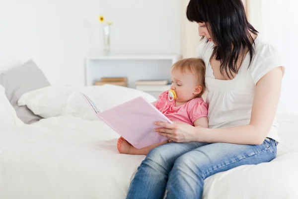Charmante brünette Frau zeigt ihrem Baby im Sitzen ein Buch — Stockfoto