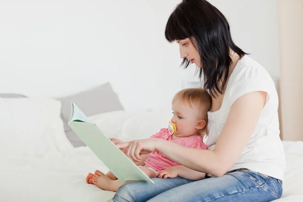 Mooie brunette vrouw tonen een boek aan haar baby terwijl vergadering o — Stockfoto