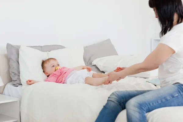 Милая брюнетка, играющая со своим ребенком, сидя на кровати — стоковое фото