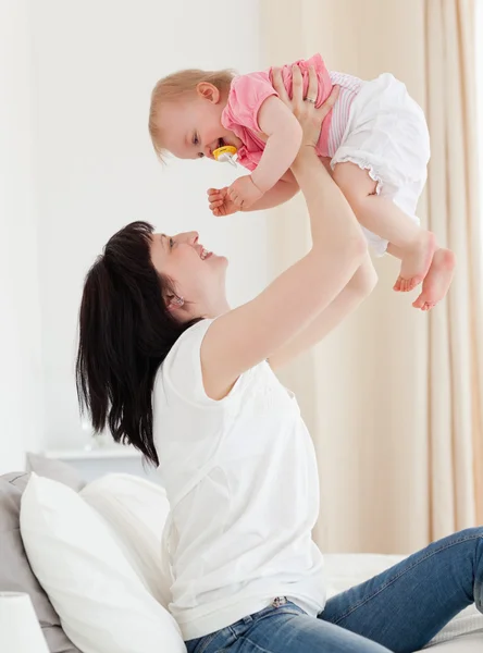 Attraktive brünette Frau spielt mit ihrem Baby, während sie auf sitzt — Stockfoto