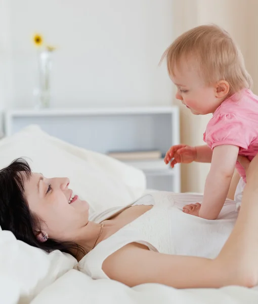 Schöne brünette Frau spielt mit ihrem Baby, während sie auf einem Bett liegt — Stockfoto