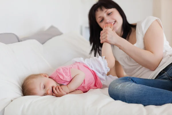 Beautiful brunette female playing with her baby while lying on a — Stock Photo, Image