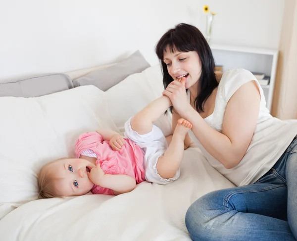 Attractive brunette female playing with her baby while lying on — Stock Photo, Image