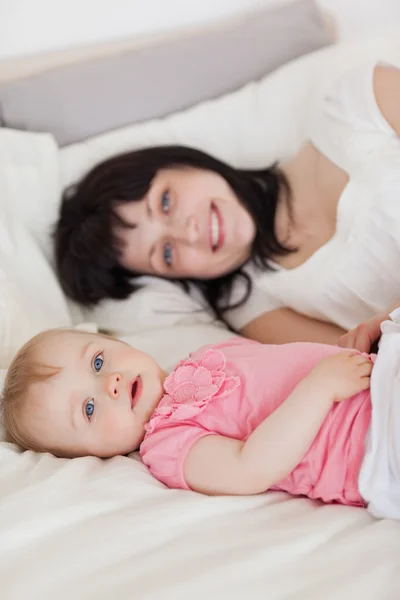 Attractive brunette female posing with her baby while lying on a — Stock Photo, Image