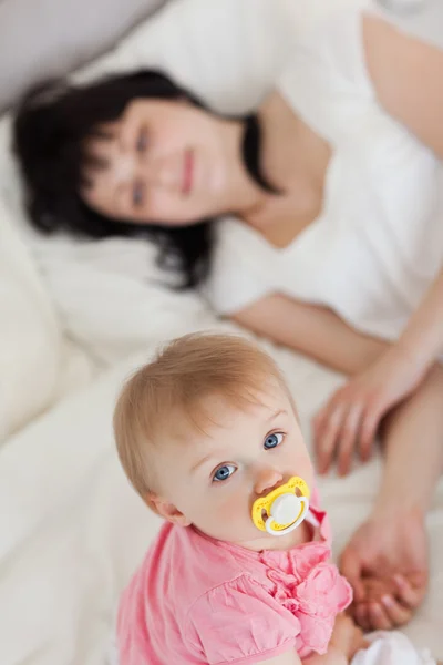 Niedliches Baby schaut in die Kamera, während ihre Mutter auf einem Bett liegt — Stockfoto