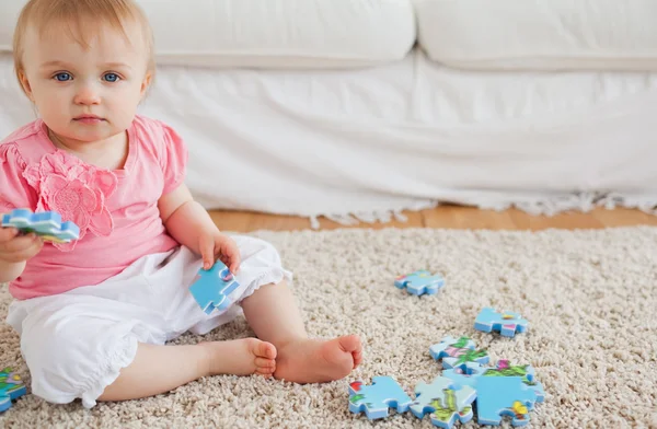 Lovely baby playing with puzzle pieces while sitting on a carpet — Stock Photo, Image