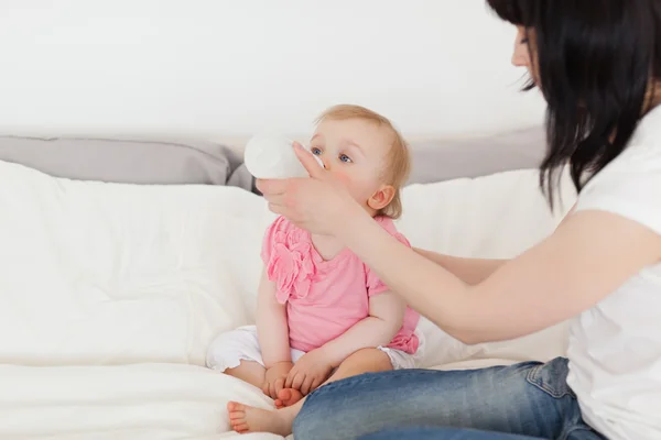 Красивая брюнетка кормит ребенка бутылкой на кровати — стоковое фото