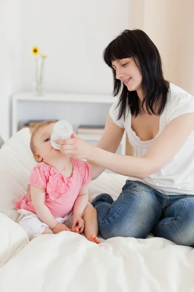 Dość brunetka kobieta karmienie za pomocą butelki swojego dziecka na łóżku — Zdjęcie stockowe