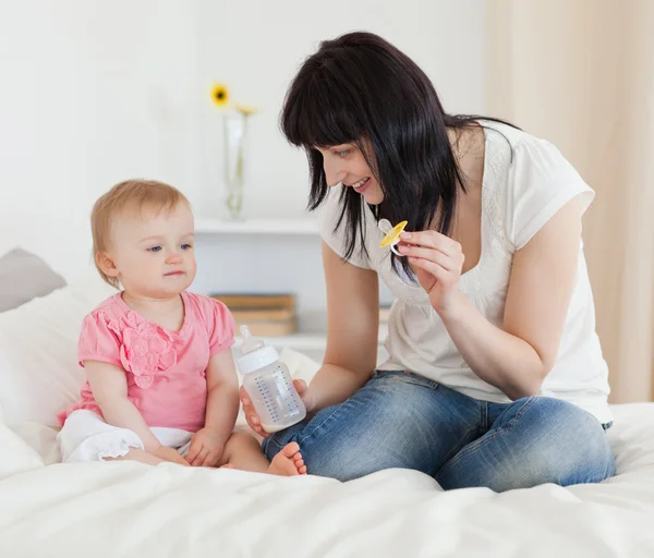 Charming brunette female showing a feeding bottle to her baby wh — Stock Photo, Image