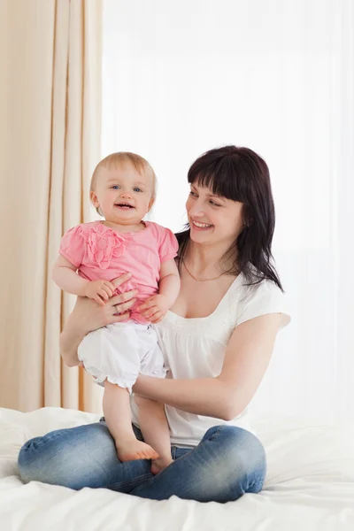 Cute brunette woman holding her baby on her knees while sitting — Stock Photo, Image