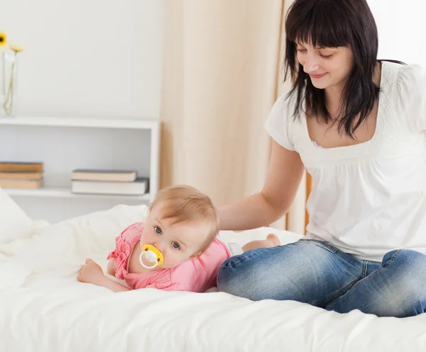 Cute brunette woman looking at her lying baby on a bed — Stock Photo, Image