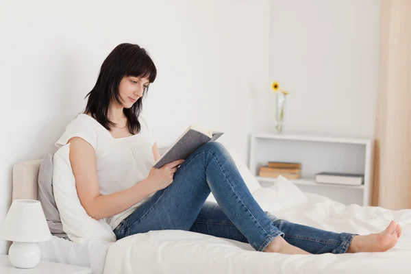아름 다운 갈색 머리 여자는 침대에 있고 있는 동안 책을 읽고 — 스톡 사진