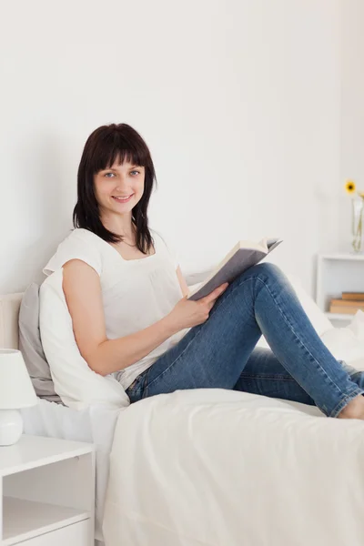 Gut aussehende brünette Frau liest ein Buch, während sie auf einem sein sitzt — Stockfoto