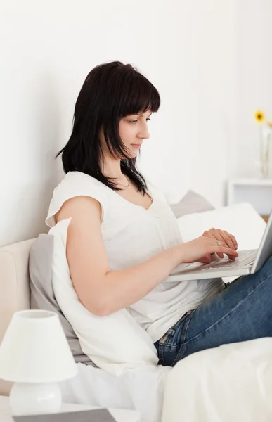 Чудова брюнетка жінка розслабляється зі своїм ноутбуком, сидячи о — стокове фото