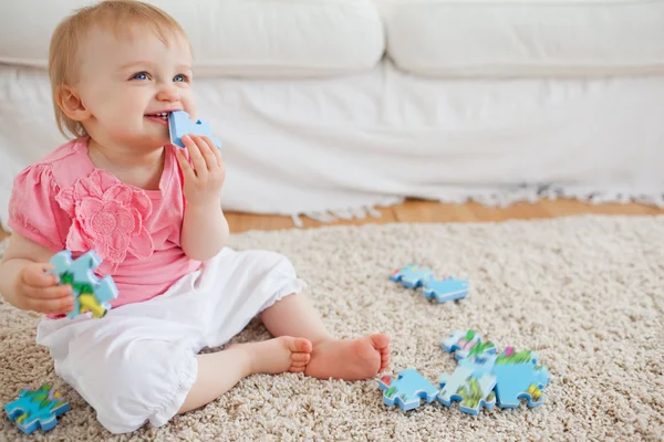 Blond baby playing with puzzle pieces while sitting on a carpet — Stock Photo, Image