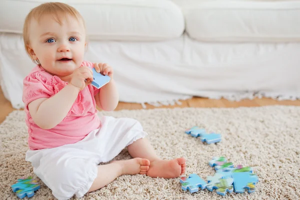 Cute blond baby playing with puzzle pieces while sitting on a ca — Stock Photo, Image
