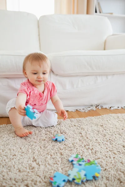 Lovely blond baby playing with puzzle pieces while sitting on a — Stock Photo, Image