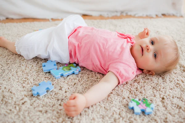 Nettes blondes Baby spielt mit Puzzleteilen, während es auf einem Karpfen liegt — Stockfoto