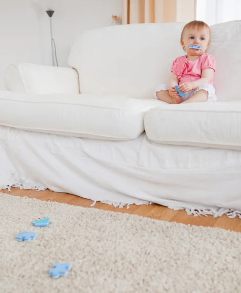 Cute blond baby playing with puzzle pieces while sitting on a so — Stock Photo, Image