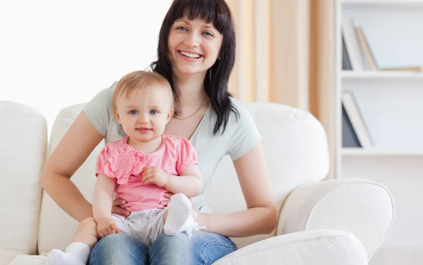 Vacker kvinna håller sitt barn i famnen medan du sitter på en sof — Stockfoto