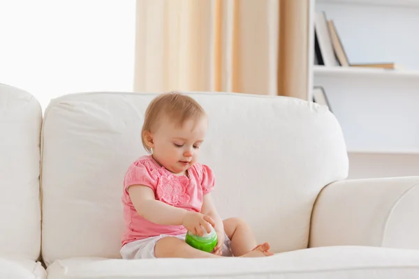 Χαριτωμένο ξανθό μωρό που παίζει με μια μπάλα, ενώ κάθεται σε έναν καναπέ — Φωτογραφία Αρχείου