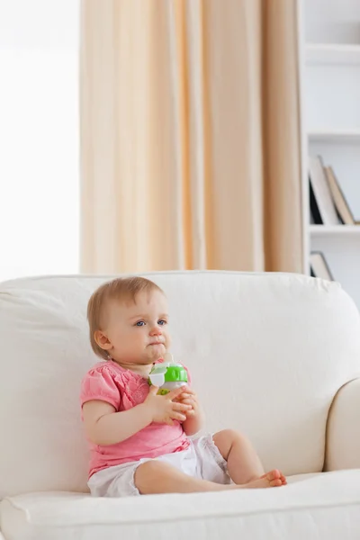 Schönes blondes Baby spielt mit einem Ball, während es auf einem Sofa sitzt — Stockfoto