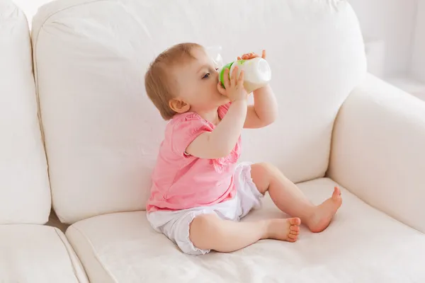 Baby bottle-feeding while sitting on a sofa — Stock Photo, Image
