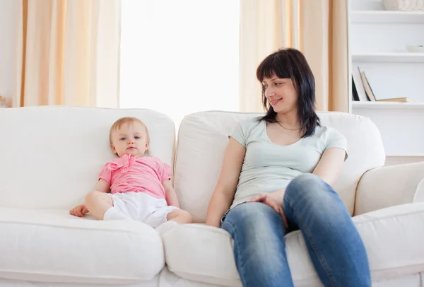 Hübsche Frau schaut ihr Baby an, während sie auf einem Sofa sitzt — Stockfoto
