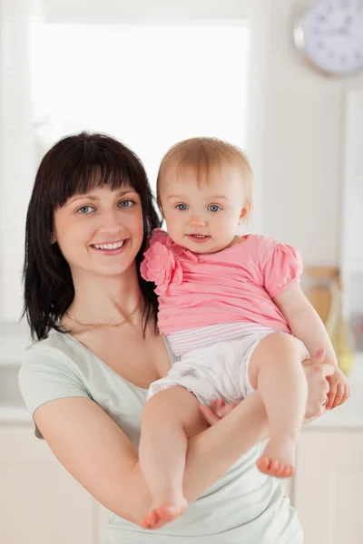 Mujer atractiva sosteniendo a su bebé en sus brazos mientras está de pie —  Fotos de Stock