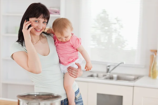 Atrakcyjna kobieta na telefon trzymając swoje dziecko w ramiona — Zdjęcie stockowe