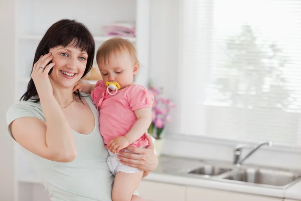 Hübsche Frau am Telefon, während sie ihr Baby im Arm hält — Stockfoto