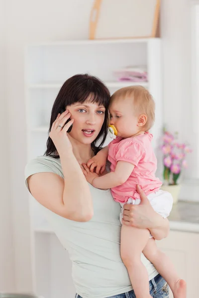 Mujer encantadora en el teléfono mientras sostiene a su bebé en sus brazos —  Fotos de Stock