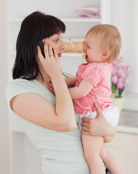 Милая женщина разговаривает по телефону, держа ребенка на руках. — стоковое фото