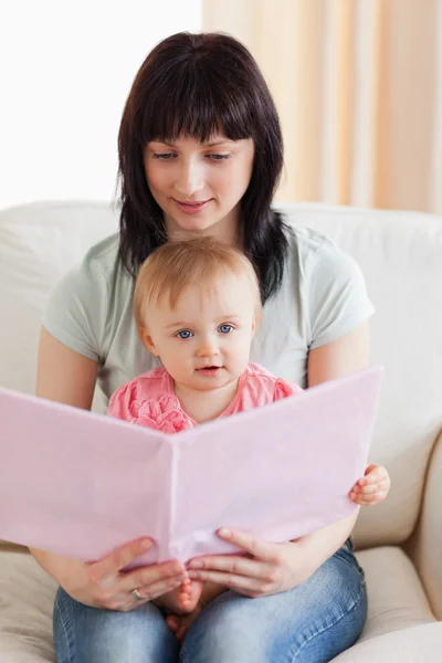 Attractive woman holding her baby and a book in her arms while s — Stock Photo, Image