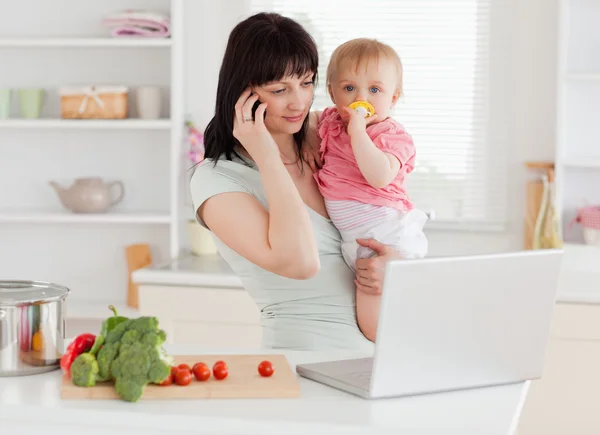 Bella donna bruna al telefono mentre tiene il suo bambino — Foto Stock