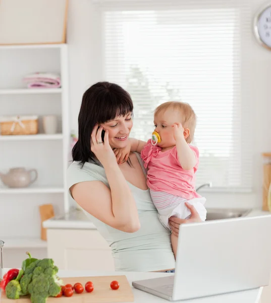 Attraente donna bruna al telefono mentre tiene in braccio il suo bambino — Foto Stock
