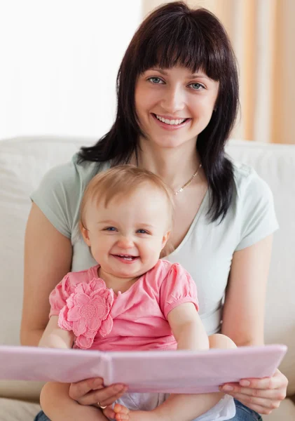 Beautiful woman holding her baby and a book in her arms while si — Stock Photo, Image