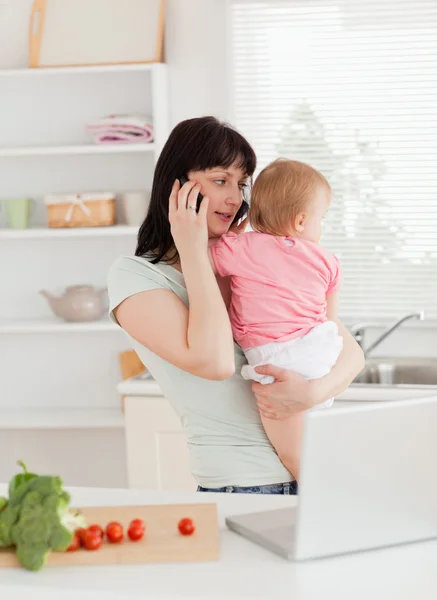 Dość brunetka kobieta na telefon trzymając dziecko w jej — Zdjęcie stockowe