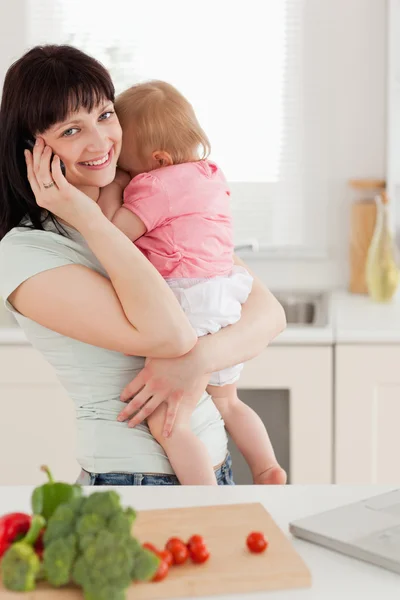 Ładny brunetka kobieta na telefon trzymając dziecko w jej — Zdjęcie stockowe