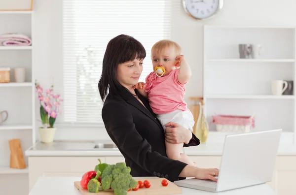 Beautiful brunette woman in suit holding her baby in her arms wh — Stock Photo, Image