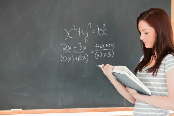 Wunderschöne Studentin betrachtet ihre Notizen beim Lösen einer Gleichung Stockbild