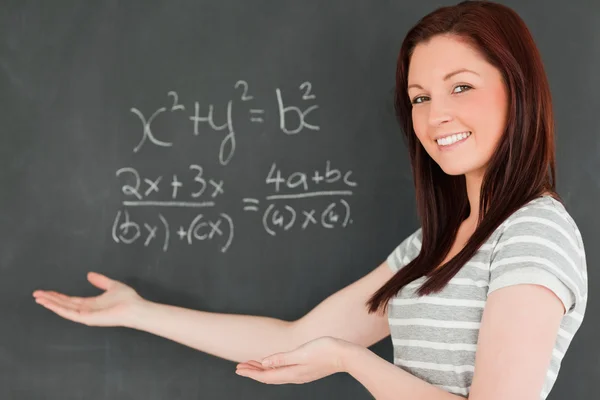 Schöne junge Frau zeigt eine Gleichung auf einer Tafel lizenzfreie Stockbilder