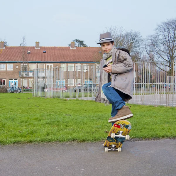 Roztomilé dospívající chlapec s mobilním telefonem dělat kaskadérské kousky na skateboardu — Stock fotografie