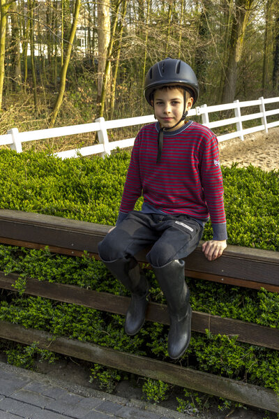 Cute teenage boy in helmet and boots for horse riding sitting n