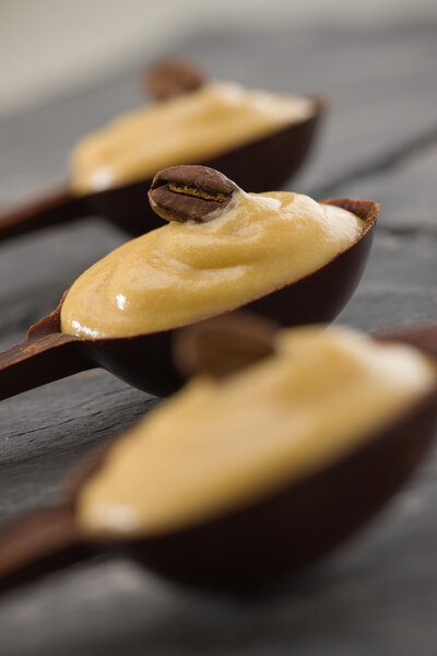 Whipped coffee mousse in a dark chocolate spoon. Very shallow depth of field. focus on the bean.