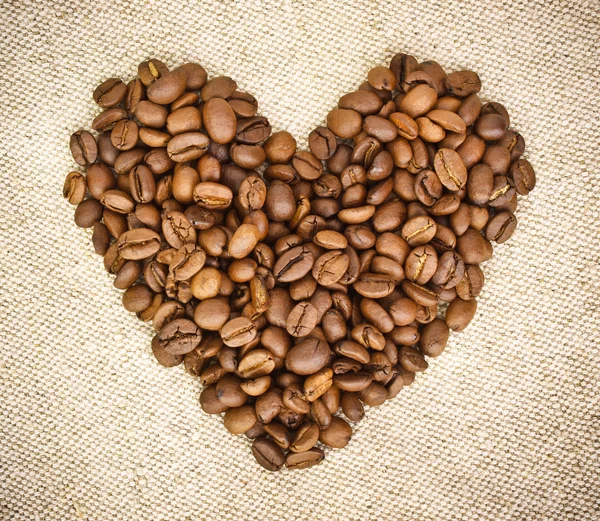 Corazón de granos de café en arpillera, fondo Hessiano — Foto de Stock