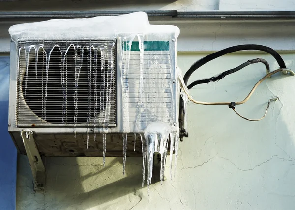 Il condizionatore d'aria coperto con ghiaccioli su una parete gialla — Foto Stock