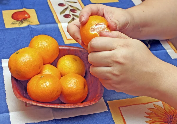 A mulher limpa tangerinas em um tecido azul — Fotografia de Stock