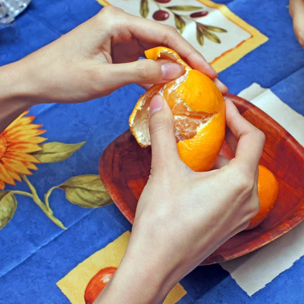 Женщина чистит мандарины на синей ткани — стоковое фото