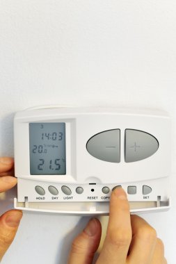 Hand pressing button on digital thermostat clipart